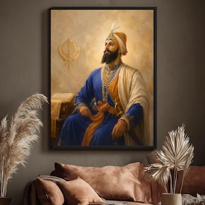 May include: A framed wall art print depicting a bearded figure wearing a blue and orange traditional outfit with a turban and a white shawl. The figure is seated beside a book, with a golden Khanda symbol visible in the background on a beige wall.
