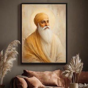 May include: A framed wall art print featuring a portrait of Guru Nanak Dev Ji. The figure wears a mustard yellow turban and matching shawl, with a long white beard and a soft, glowing golden halo against a textured, neutral-toned background.
