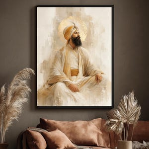 May include: A framed wall art print depicting a bearded person wearing a cream-colored turban and flowing robes in shades of white and gold. The figure is seated in a meditative pose against a soft, textured background with a golden halo effect.
