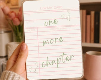 May include: A clear phone case with a library card design. The card features pink lines and the words "one more chapter" in green script. Small green hearts are scattered around the text. The case is held in a hand.