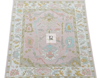 May include: A rectangular, pink rug with an intricate floral design. The rug features a central medallion and a border with repeating patterns in shades of pink, green, blue, and gold. The rug is made of a soft material.
