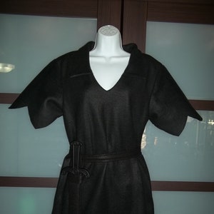 May include: Black tunic-style costume with a V-neck and short sleeves. The costume has a matching belt and a decorative sword attached. The bottom of the tunic has a unique pointed design. The costume is displayed on a white mannequin.