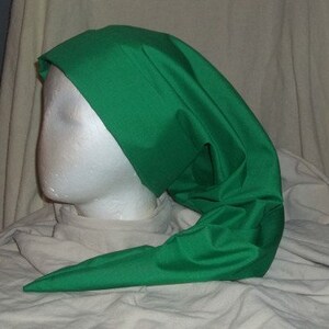 Puede incluir: Un sombrero verde brillante con un extremo largo y puntiagudo. El sombrero, hecho de una tela lisa y brillante, est&aacute; drapeado sobre una cabeza de maniqu&iacute; blanca. El dise&ntilde;o del sombrero recuerda a un estilo medieval o de fantas&iacute;a.