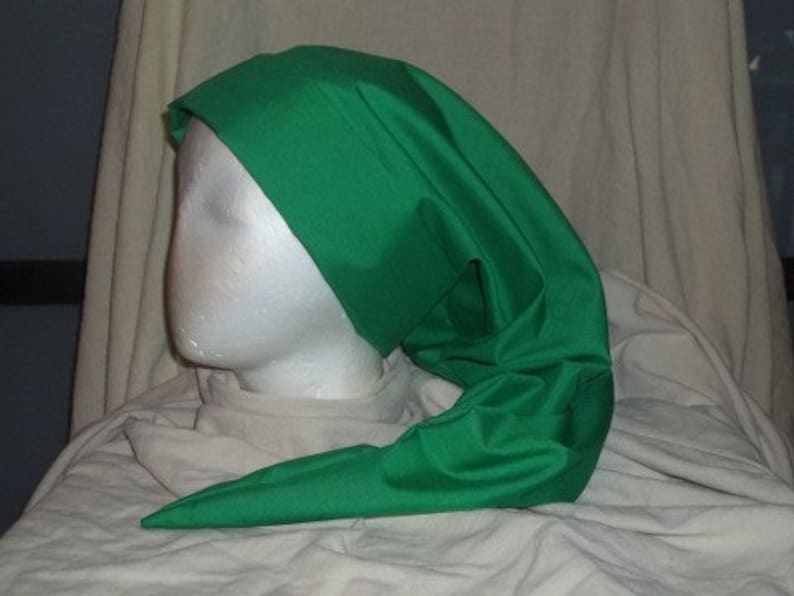 Puede incluir: Un sombrero verde brillante con un extremo largo y puntiagudo. El sombrero, hecho de una tela lisa y brillante, est&aacute; drapeado sobre una cabeza de maniqu&iacute; blanca. El dise&ntilde;o del sombrero recuerda a un estilo medieval o de fantas&iacute;a.