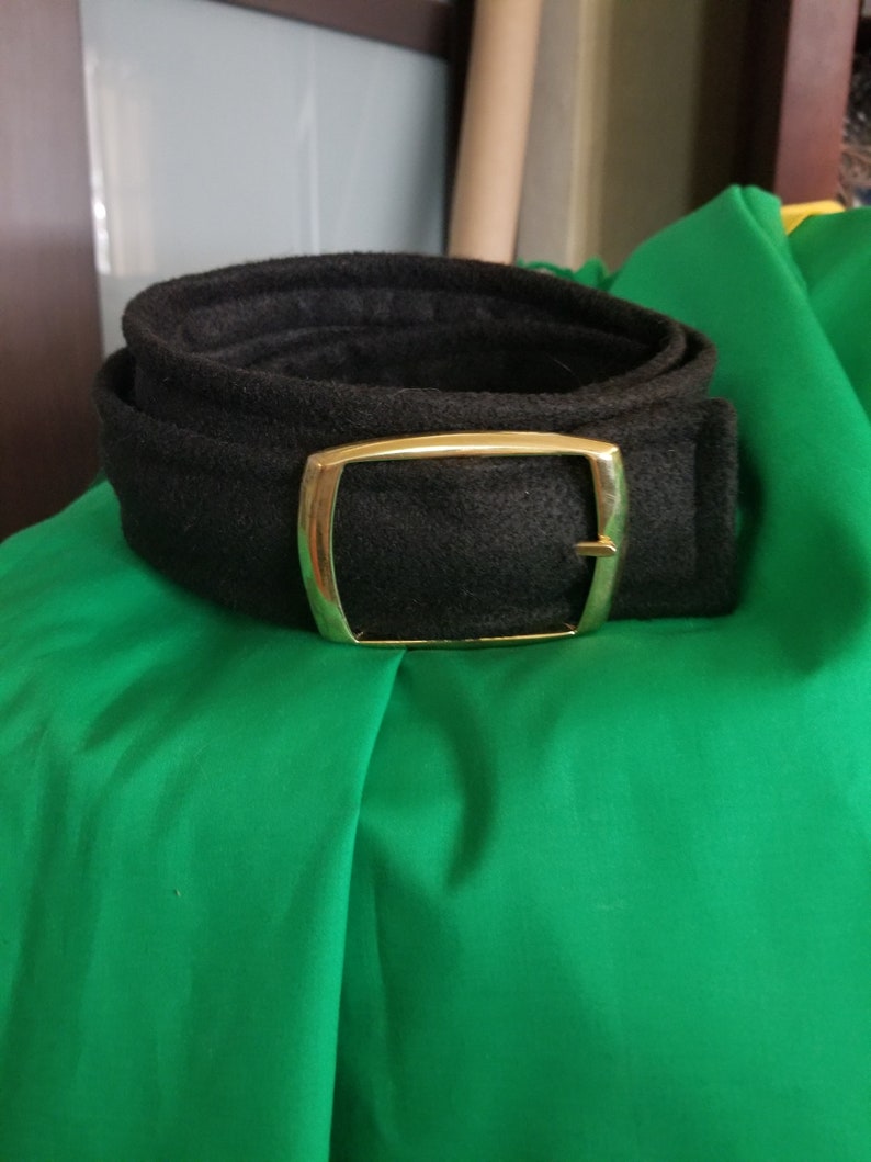 Pode incluir: Um cinto preto com fivela dourada enrolado sobre tecido verde. O cinto &eacute; feito de material texturizado. A fivela &eacute; retangular com cantos arredondados.
