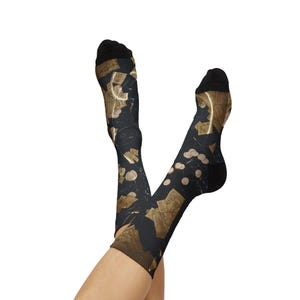 May include: A pair of black crew socks featuring an all-over print of vintage-style tan paper documents, letters, and circular gold coins scattered across the dark fabric. The socks have solid black cuffs, heels, and toe sections for contrast.