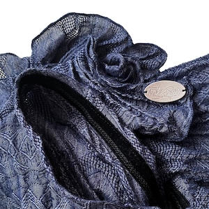May include: A close-up of a navy blue knitted fabric with a decorative flower detail. The fabric has a textured pattern and a black zipper. The fabric has a label that says "The Shabby Rose Collection".