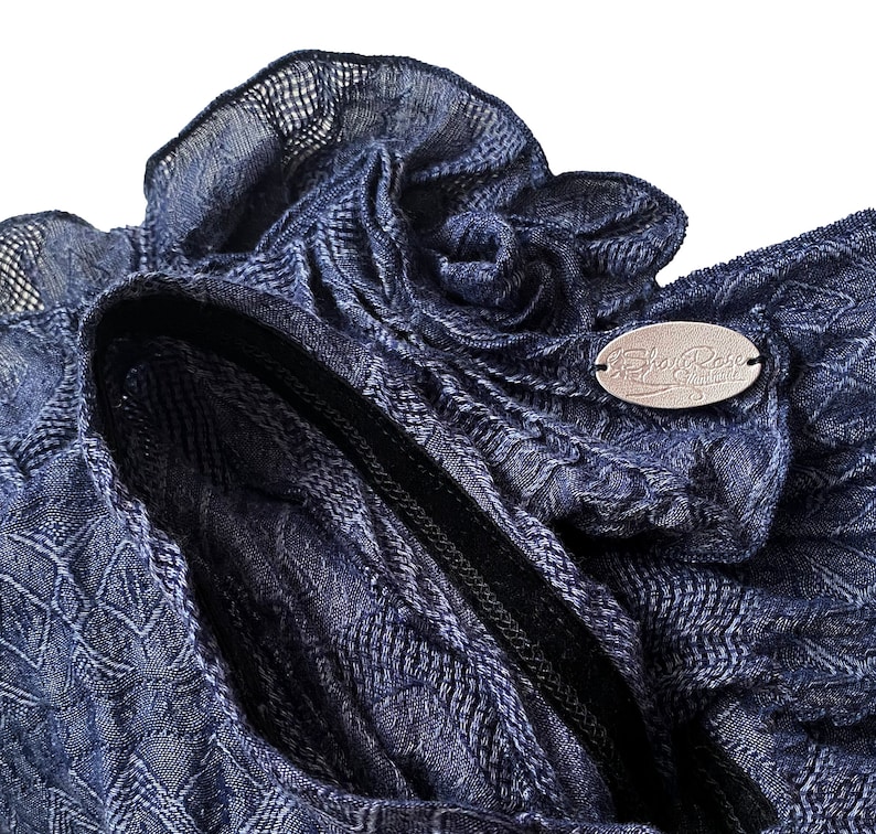 May include: A close-up of a navy blue knitted fabric with a decorative flower detail. The fabric has a textured pattern and a black zipper. The fabric has a label that says "The Shabby Rose Collection".