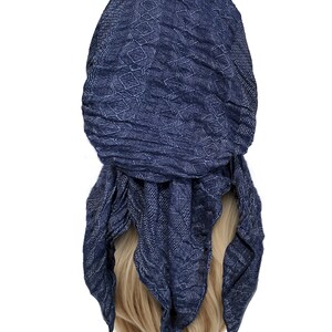 May include: A navy blue patterned headscarf with a geometric design. The scarf is tied in a knot at the back of the head and the ends are hanging down.