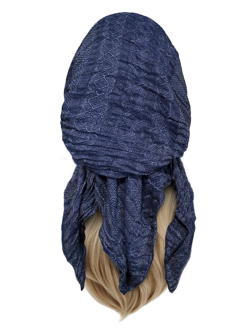 May include: A navy blue patterned headscarf with a geometric design. The scarf is tied in a knot at the back of the head and the ends are hanging down.