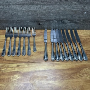 May include: A collection of vintage silverware, including forks and knives, arranged on a wooden surface. The silverware has a decorative beaded design on the handles. The forks and knives are made of a shiny, silver-colored metal.
