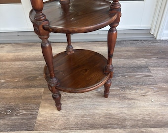 May include: A two-tiered, dark brown wooden plant stand with a glossy finish. The stand features two circular shelves supported by turned legs and a central column. The stand is approximately 30 inches tall.