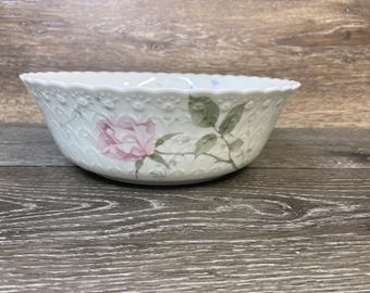 May include: White porcelain bowl with a scalloped rim and a floral rose design. The bowl features a pink rose with green leaves and stems. The bowl has a textured surface.