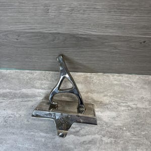 Puede incluir: Un colgador de calcetín plateado con un diseño arqueado y una base rectangular. El colgador tiene un gancho en la parte inferior para colgar calcetines navideños. El metal tiene un acabado brillante.