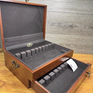 May include: A wooden cutlery chest with a dark brown finish, featuring an open hinged lid and a pull-out drawer. Both the interior and the drawer are lined with dark grey fabric and include slotted dividers for organising flatware.