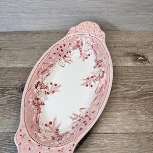 May include: Oval serving dish with a white center and a pink floral border. The pink border features a repeating pattern and a decorative floral design. The dish has handles on each end.