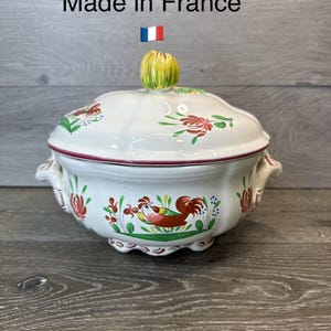 May include: White ceramic soup tureen with a lid, featuring hand-painted red and green floral and rooster designs. The tureen has a red rim and two handles. The lid has a yellow and green knob. Text on the image says "Made in France".