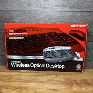Könnte beinhalten: Eine Microsoft Wireless Optical Desktop Verpackung mit einer schwarz-silbernen Multimedia-Tastatur und einer passenden kabellosen optischen Maus. Die rot-schwarze Schachtel zeigt den Produktnamen und Text zu den Funktionen der Geräte.