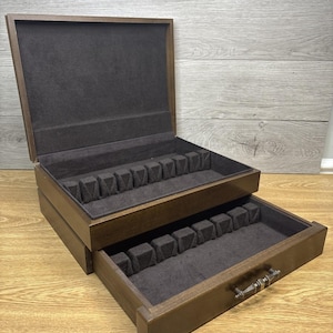 May include: A wooden silverware chest with a dark brown finish. The chest has two levels, with a drawer pulled out, revealing compartments lined with dark gray fabric. The top lid is open, showing a similar interior.