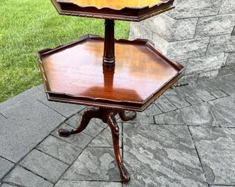 May include: A two-tiered, antique mahogany side table. The table has a hexagonal top and bottom with a scalloped edge. The table stands on three carved legs. The table is approximately 28 inches tall.
