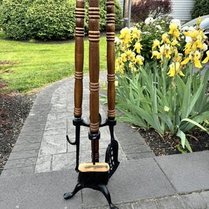 May include: A vintage fireplace tool set with a black cast iron base and three wooden handled tools. The tools include a poker, shovel, and brush. The wooden handles are a dark brown color.