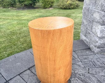 May include: A cylindrical wooden stool with a light brown finish. The stool has a flat top and a slightly wider base. It is approximately 18 inches tall and sits on a gray stone patio.