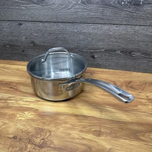 Puede incluir: Cacerola de acero inoxidable con tapa de cristal y mango largo. La sartén tiene la marca "VIKING" estampada en el lateral. La sartén está sobre una superficie de madera.