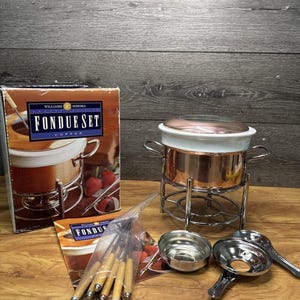 May include: A white ceramic mug with a black handle and the text "But First, Coffee" in a bold, black font. The mug is set against a blurred background, suggesting a cosy setting.