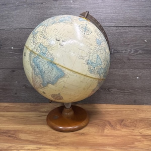 Może przedstawiać: Zabytkowy globus z kremową powierzchnią, przedstawiający kontynenty w kolorze niebieskim i beżowym. Posiada drewnianą podstawę i metalowy pierścień południkowy. Globus to klasyczne narzędzie edukacyjne i element dekoracyjny.