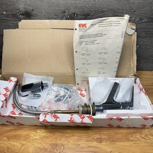 May include: A chrome kitchen faucet with a pull-out hand shower, flexible metal hose, and brass mounting hardware, packaged in a branded KWC cardboard box with an included instruction manual featuring technical diagrams and the KWC logo.