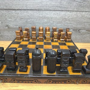 May include: A wooden chess set with a black and brown color scheme. The chess pieces are carved with a unique design, and the board has a checkerboard pattern. The set is displayed on a wooden surface.