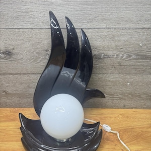 May include: A black ceramic table lamp featuring a glossy finish and a sculptural, flame-like silhouette. The base supports a spherical white glass globe light bulb. A white electrical cord with an inline switch extends from the lamp base.