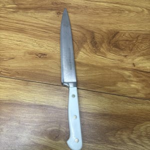 May include: A kitchen knife with a pointed silver stainless steel blade and a white handle secured by three visible metal rivets. The blade features a straight edge and a sharp tip, while the handle is smooth with a curved ergonomic shape.