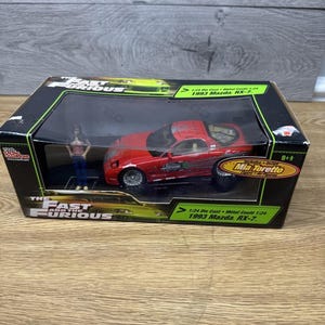 Può includere: Un'auto modello Mazda RX-7 rossa del 1993 pressofusa in una scatola nera e verde. La scatola presenta il testo "The Fast and the Furious" e "Mia Toretto". Il modello è in scala 1:24.