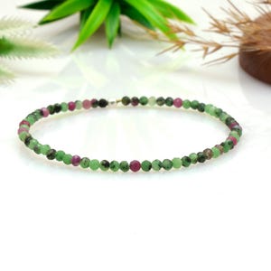以下が含まれることがあります： 緑、ピンク、濃いグレーの色合いの小さなファセットビーズで構成された繊細なブレスレット。ビーズはつながっており、円形を形成しています。ブレスレットはおそらく宝石で作られており、手首に着用するように設計されています。