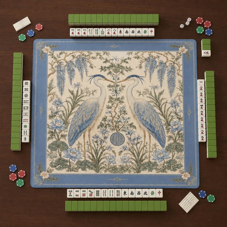 May include: A square mahjong mat featuring a central illustration of two herons facing each other amidst wisteria and lotus flowers, framed by a blue border. The mat is surrounded by rows of green and white mahjong tiles and colorful game chips.