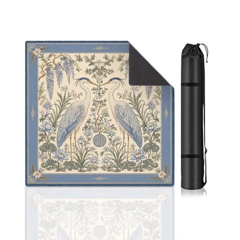 May include: A square mat featuring a symmetrical illustration of two herons facing each other amidst blue and cream floral patterns, including wisteria and lotus flowers, with a dark blue border and a matching black cylindrical carrying case.