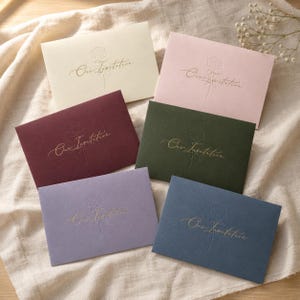 Pode incluir: Seis envelopes retangulares nas cores creme, rosa claro, bordô, verde escuro, lavanda e azul marinho. Cada envelope apresenta uma ilustração de rosa em relevo dourado e o texto Our Invitation em letra cursiva no centro.