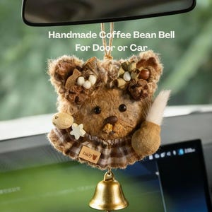 Puede incluir: Campana artesanal de granos de café para puerta o coche. La campana tiene forma de oso de peluche con una textura marrón similar a la piel, adornada con elementos decorativos. Una pequeña campana dorada cuelga debajo. El texto "Handmade Coffee Bean Bell For Door or Car" es visible.