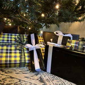 Könnte beinhalten: Mehrere verpackte Geschenke unter einem Weihnachtsbaum. Die Geschenke sind in schwarzes, gelb kariertes und schwarzes Papier mit weißen Bändern verpackt. Der Baum ist grün mit kleinen weißen Lichtern.