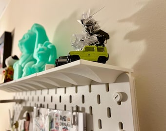 May include: A white shelf displays a collection of items. A lime green toy SUV sits next to a clear robot figure. A turquoise sculpture and other small items are also on the shelf. The shelf is mounted on a white pegboard.