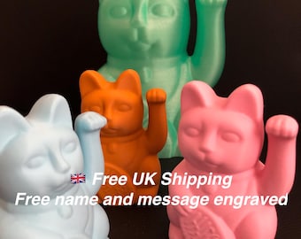 May include: Four colorful Maneki Neko figurines in shades of blue, orange, pink, and green. Each cat is in a seated position with one paw raised. The background is a solid black.