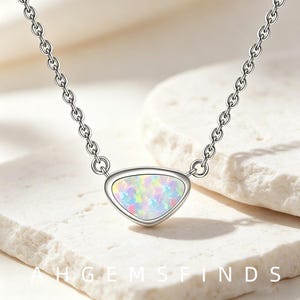 May include: A silver-toned necklace featuring a triangular pendant with a smooth metal border and an iridescent, multi-colored opal-like inlay. The pendant is attached to a delicate silver-toned chain with small, uniform circular links.