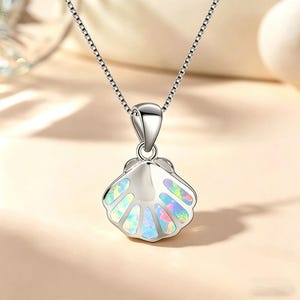 May include: A silver seashell pendant necklace. The pendant features a detailed shell design with iridescent opal-like accents. The necklace has a delicate chain, perfect for everyday wear.