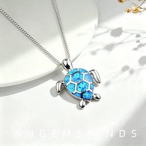 May include: A silver-toned necklace featuring a turtle-shaped pendant with a bright blue, iridescent, mosaic-style inlay on its shell. The pendant is attached to a delicate silver chain. The text AHGEMSFINDS is visible at the bottom of the image.