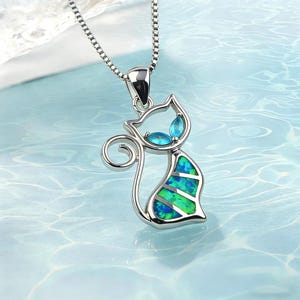 May include: A silver cat pendant necklace with a blue and green opal design. The cat-shaped pendant has blue gemstone accents for the eyes. The necklace is on a silver chain.