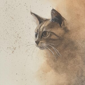 Puede incluir: Pintura a la acuarela del perfil de un gato, en tonos marrones y beige. El pelaje del gato está detallado con sutiles pinceladas, y sus bigotes están delicadamente dibujados. La obra de arte tiene un fondo suave y difuso con salpicaduras de pintura.