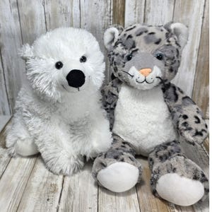 May include: Two plush stuffed animals consisting of a white polar bear with a black nose and a grey and white snow leopard with dark spots, a pink nose, and long whiskers. Both toys feature soft, fuzzy fur and are seated in an upright position.