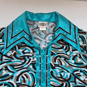 May include: A turquoise and black zip-up shirt featuring a geometric pattern of interlocking circles in shades of turquoise, black, white, and tan. The collar and front placket are accented with silver rhinestones and black trim. A Rod's label is visible.