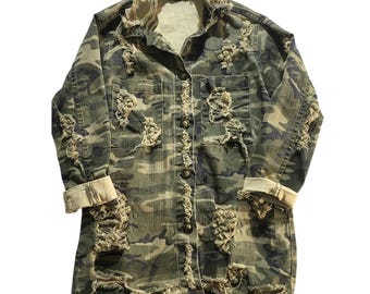 May include: A long-sleeved camouflage jacket featuring a distressed, frayed aesthetic with multiple rips and tears across the front. The garment includes a button-down front closure, two chest pockets, and light-colored cuffs on the sleeves.